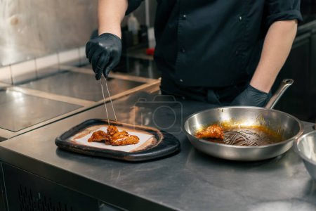 Téléchargez les photos : Close-up dans une cuisine professionnelle le chef met des ailes de poulet prêtes à l'emploi sur un plateau en bois - en image libre de droit