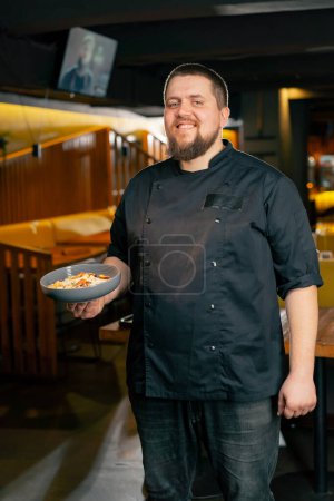 in a restaurant a chef in a black jacket stands with a prepared salad smiles looks at the camera