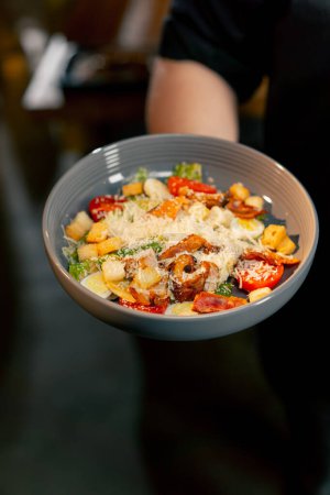 Téléchargez les photos : Gros plan dans un chef de restaurant dans une veste noire se tient sourire avec une salade préparée - en image libre de droit