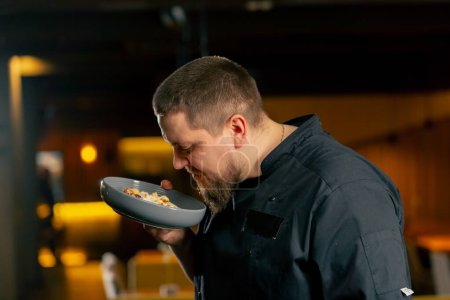 Téléchargez les photos : Un chef en noir dans un restaurant renifle la salade César qu'il a lui-même préparée - en image libre de droit