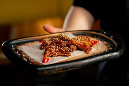 Téléchargez les photos : Main dans la main dans un chef de restaurant dans une veste noire stands avec une préparé ailes de poulet - en image libre de droit