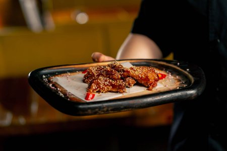 Téléchargez les photos : Main dans la main dans un chef de restaurant dans une veste noire stands avec une préparé ailes de poulet - en image libre de droit