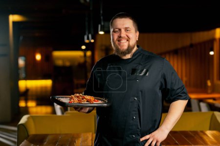 Photo for In a restaurant chef in a black jacket stands smiling with a prepared Chicken wings - Royalty Free Image