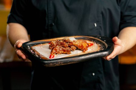 close up hand in a restaurant chef in a black jacket stands with a prepared Chicken wings