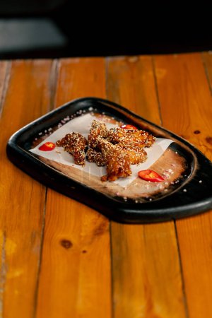 Foto de Primer plano sobre una mesa de madera hay un plato preparado de alas de pollo con semillas de sésamo - Imagen libre de derechos