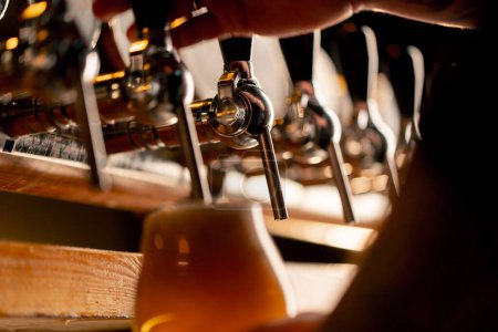 Foto de Primer plano en la sala de cerveza en el mostrador del bar las manos de los camareros vierten cerveza ligera en un vaso - Imagen libre de derechos