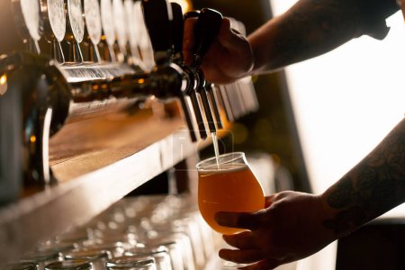 Foto de Primer plano en la sala de cerveza en el mostrador del bar las manos de los camareros vierten cerveza ligera en un vaso - Imagen libre de derechos