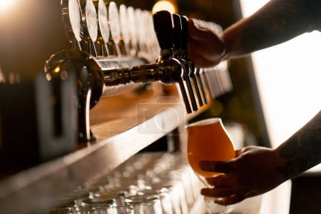 Téléchargez les photos : Gros plan dans la brasserie au comptoir du bar les mains des barmans versent de la bière légère dans un verre - en image libre de droit