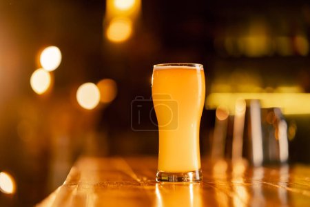 Téléchargez les photos : Fermer dans le bar il y a un verre de bière sur un comptoir de bar en bois dans les rayons du soleil - en image libre de droit