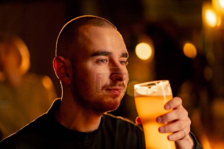 Téléchargez les photos : Gros plan sur une table de bar en bois un gars boit dans un verre de bière lumière lumière d'éclairage chaud - en image libre de droit