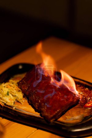 Photo for Close-up in a professional kitchen a finished rib on a tray flames on the ribs - Royalty Free Image