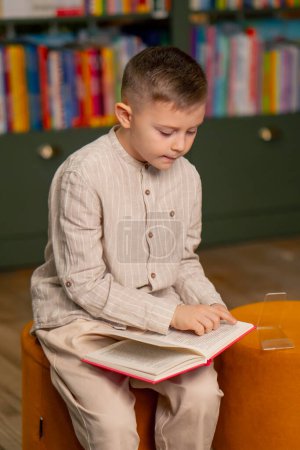Foto de En una librería en el área de los niños un niño guapo con ropa ligera lee un libro - Imagen libre de derechos