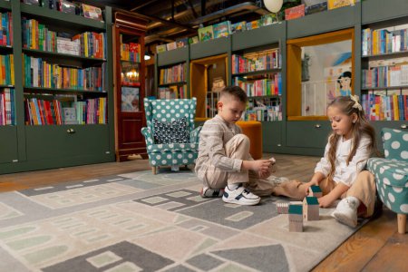 Foto de En una librería en el área de niños hermosa chica de pelo largo y niño jugar con juguetes de madera - Imagen libre de derechos
