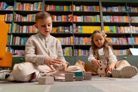 Foto de Primer plano en una librería en el área de niños hermosa chica de pelo largo y niño jugar con juguetes de madera - Imagen libre de derechos
