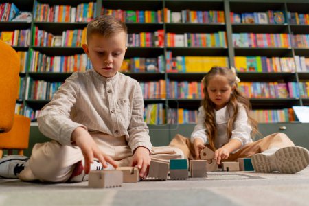 Photo for Close up in a bookstore in the children area beautiful long-haired girl and boy play with wooden toys - Royalty Free Image