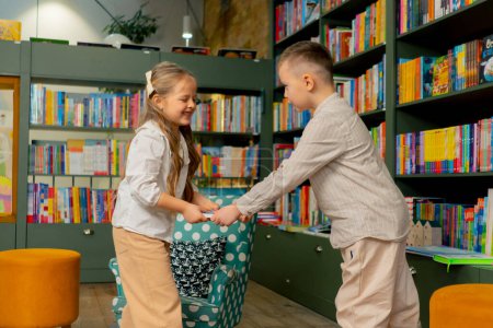 Téléchargez les photos : Dans une librairie dans la zone des enfants une belle fille et un garçon se battent pour un livre - en image libre de droit