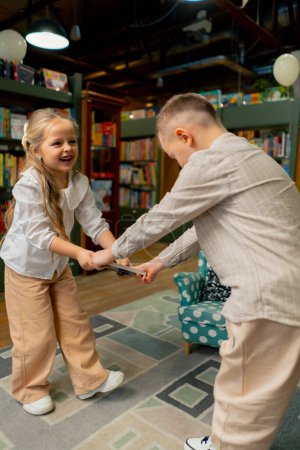 Téléchargez les photos : Dans une librairie dans la zone des enfants une belle fille et un garçon se battent pour un livre - en image libre de droit