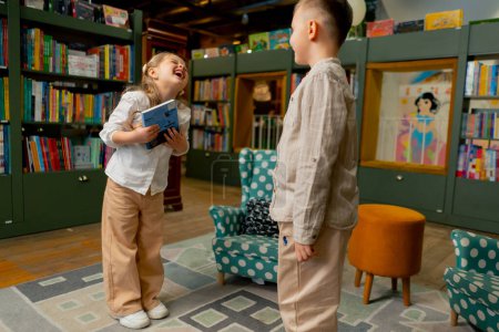 Photo for In a bookstore in the children area a beautiful girl and a boy fight for one book - Royalty Free Image