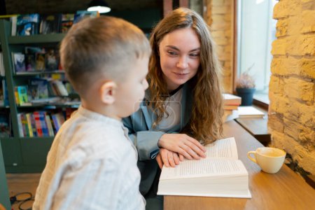 Photo for Close up in a bookstore near the window a young mother sits teaching her son to read child development - Royalty Free Image