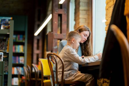Photo for In a bookstore near the window a young mother sits teaching her son to read child development - Royalty Free Image