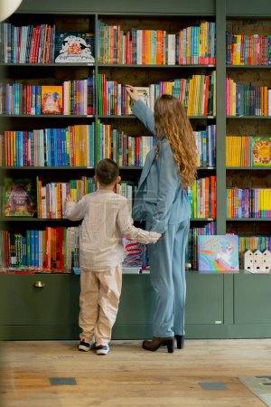 Photo for In a bookstore a young mother with her son is looking for a book for reading practice - Royalty Free Image