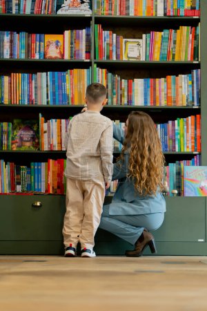 in a bookstore a young mother with her son is looking for a book for reading practice