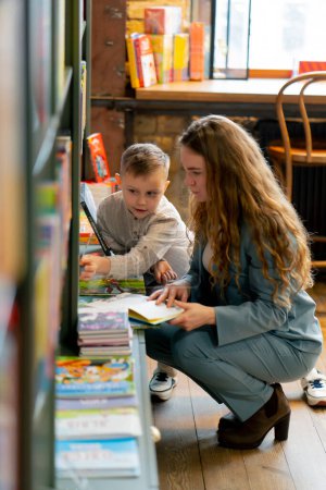 in a bookstore a young mother with her son is looking for a book for reading practice