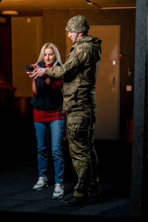 in a professional shooting range a military man tells and shows a girl what the correct stance with a pistol is