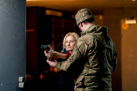 Photo for In a professional shooting range a military man tells and shows a girl what the correct stance with a pistol is - Royalty Free Image