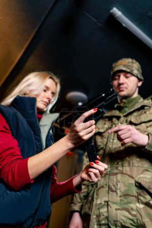 Foto de Tiro bajo en un campo de tiro profesional un militar le dice y muestra a una chica la postura correcta con una pistola es - Imagen libre de derechos