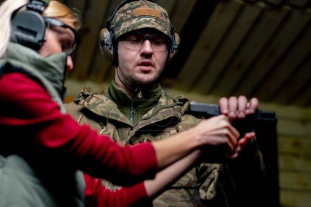 Foto de En un campo de tiro profesional un militar le dice y le muestra a una chica cómo recargar una pistola - Imagen libre de derechos