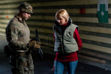 Foto de En un campo de tiro profesional un entrenador militar le dice a una chica cómo manejar correctamente las armas de la OTAN - Imagen libre de derechos