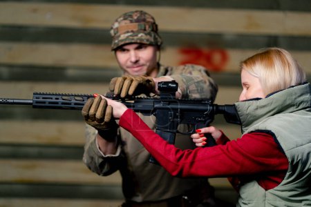 At a professional shooting range a military trainer teaches a cheap girl how to hold a NATO rifle correctly