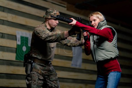 Foto de En un campo de tiro profesional, un entrenador militar enseña a una chica barata a sostener correctamente un rifle de la OTAN. - Imagen libre de derechos