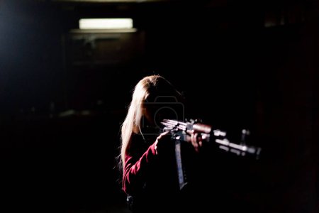 Foto de Estrategia táctica militar chica se para con un rifle apuntando en el contraste oscuro luz trasera silueta - Imagen libre de derechos