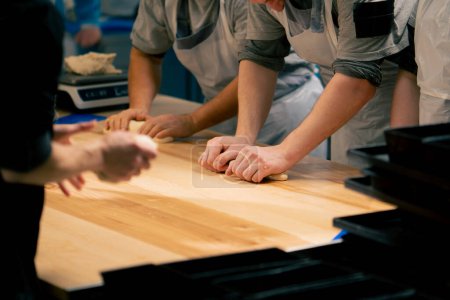 Photo for Layout in a professional kitchen a group of bakers at the table process the dough and form it into a mold - Royalty Free Image