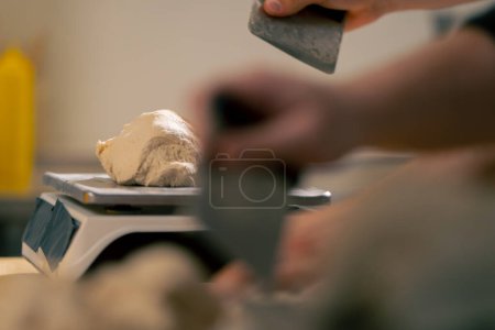 Photo for Close-up of a baker cutting off excess dough on a scale in a professional kitchen - Royalty Free Image