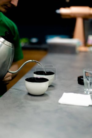 Foto de Primer plano en una fábrica de tostado de café un probador se para en la cocina y vierte agua hirviendo en tazones de café - Imagen libre de derechos