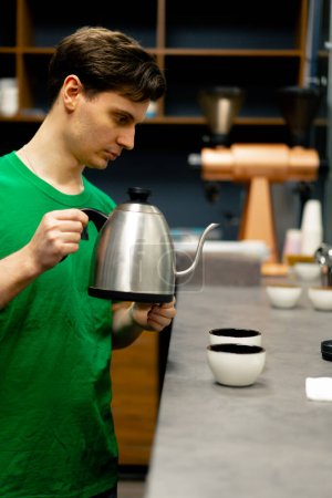 Foto de En una fábrica de tostado de café un probador está en la cocina con una tetera de agua hirviendo a punto de verter - Imagen libre de derechos