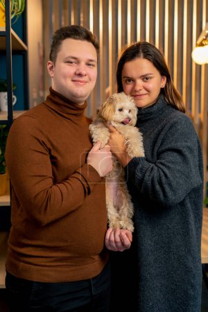 Téléchargez les photos : Lapdog un couple amoureux se tient étreignant un chien tient fermement dans leurs bras photo de famille dans la bouillie - en image libre de droit