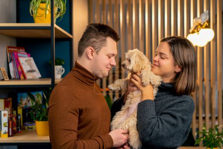 Téléchargez les photos : Lapdog un couple amoureux se tient étreignant un chien tient fermement dans leurs bras photo de famille dans la bouillie - en image libre de droit