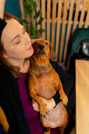 family photo with a small dachshund in the arms of the owner in a cafe they hug and play