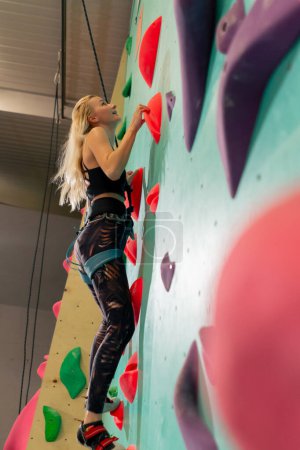 Foto de En la pared de escalada una joven sube la pared por primera vez, el entrenador de abajo con una cuerda de seguridad - Imagen libre de derechos