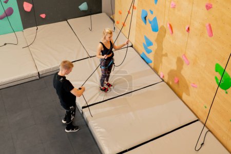 Photo for At the climbing wall a young girl goes down the safety rope, the coach insures against falling - Royalty Free Image