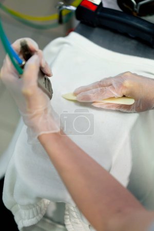 Photo for Close up top shot professional dry cleaner a young girl removes a stain using a special chemical pencil with a steamer - Royalty Free Image