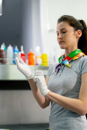 Téléchargez les photos : Nettoyeur professionnel à sec, une jeune fille met des gants en tissu blanc pour la propreté du travail - en image libre de droit