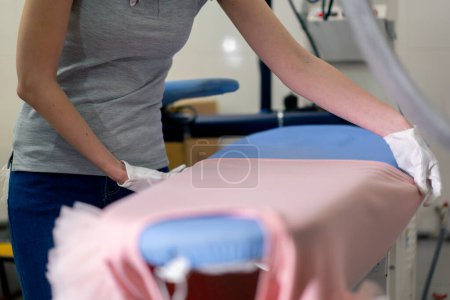 Téléchargez les photos : Close-up professionnel nettoyage à sec jeune fille pose une veste rose pour le matériel professionnel de repassage - en image libre de droit