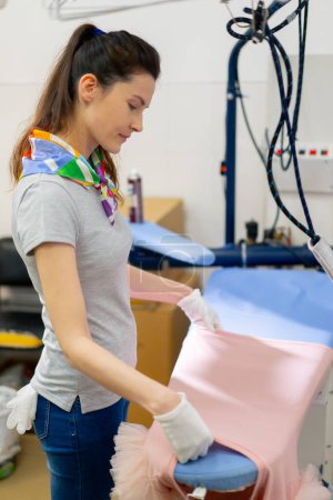 Téléchargez les photos : Nettoyage à sec professionnel jeune fille pose une veste rose pour le matériel professionnel de repassage - en image libre de droit