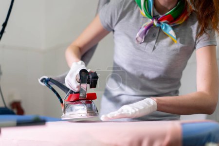 Photo for Professional dry cleaning young girl ironing pink with professional iron with steam - Royalty Free Image