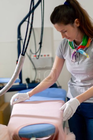 Téléchargez les photos : Professional dry cleaning young girl lays out a pink jacket for ironing professional equipment - en image libre de droit
